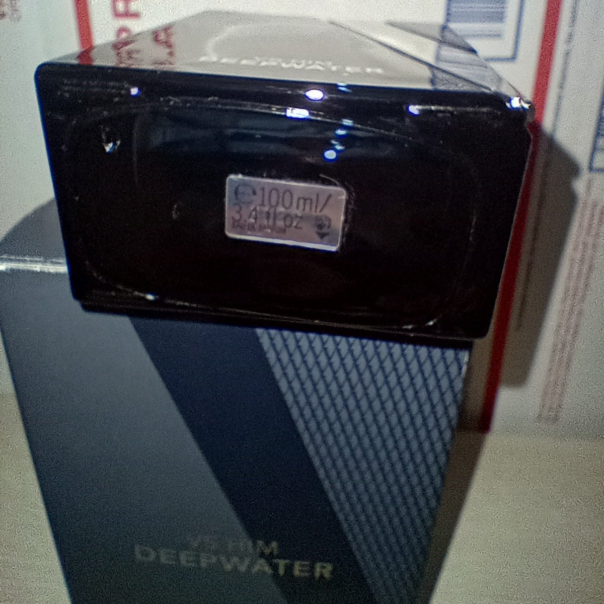 A dark glossy rectangular perfume bottle with a small silver label reading 100ml, placed on top of its dark blue and gray box. The box has the brand name Deepwater visible on the side.
