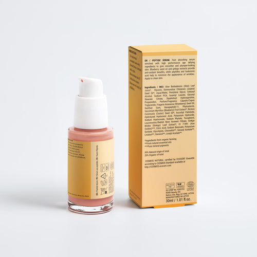 A small cosmetic bottle with a white pump and a peach-pink product inside, standing next to its tall yellow box on a clean light gray studio background.